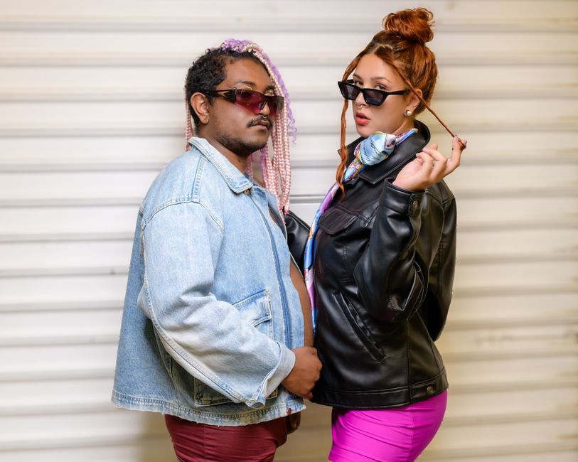 Fashionable couple wearing sunglasses, posing confidently in stylish denim and leather jackets.