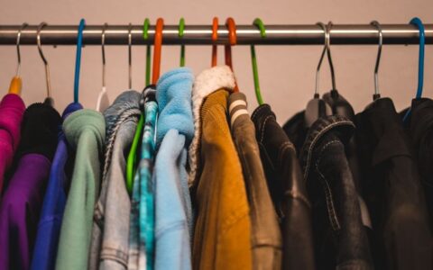 Close-up of various colorful jackets on hangers in a closet setting.