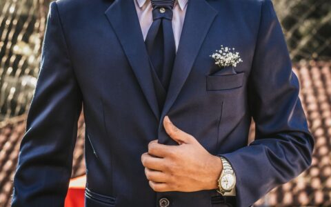 Adult man in a navy suit adjusting his tie, showcasing formal elegance outdoors.