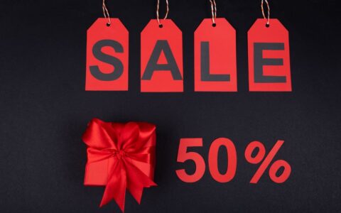 Red gift box next to sale tags and 50% sign on black background, ideal for promotions.