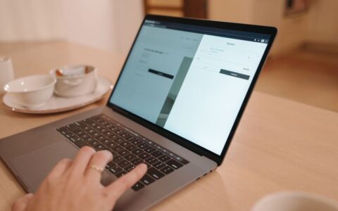 A close-up view of a person using a laptop on a wooden table indoors, creating a warm and professional atmosphere.