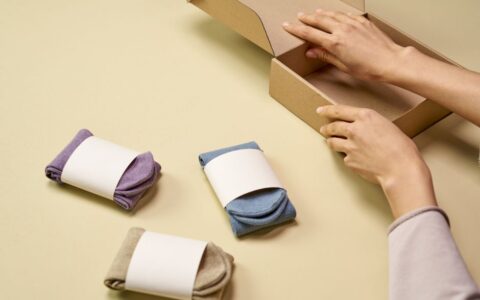 Hands packaging colorful socks into a cardboard box for shipment or storage.