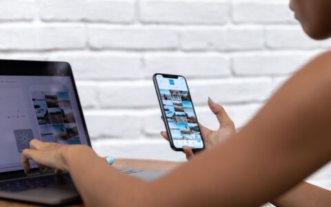 A woman working remotely using a laptop and smartphone, focusing on social media content.
